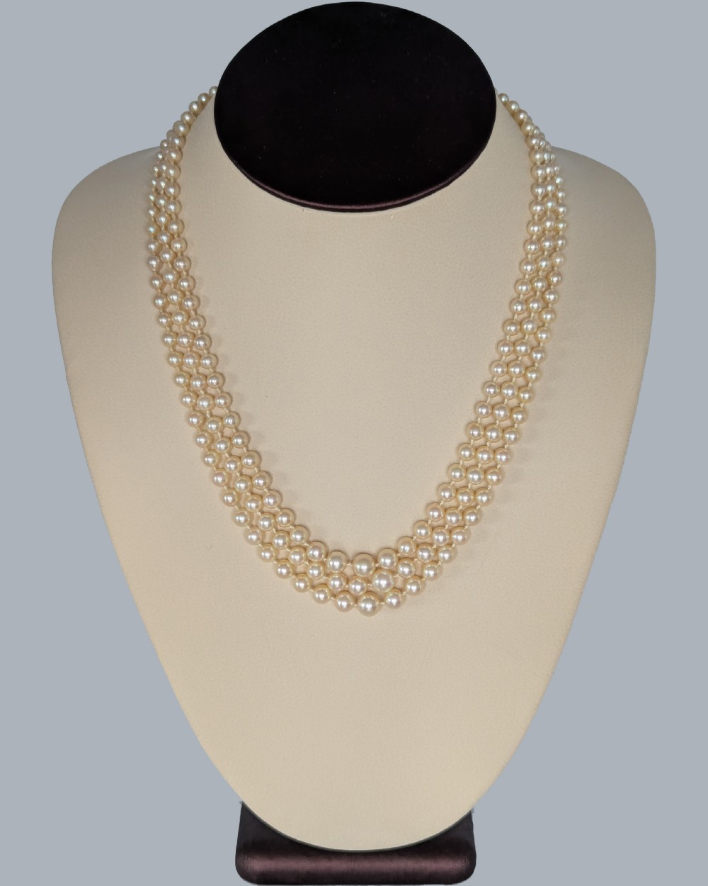 A 1950s triple strand pearl necklace featuring graduated cream pearls and a geometric diamond-set clasp with a safety chain. View IX