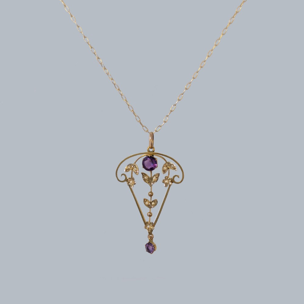 An Edwardian 9ct gold openwork pendant featuring set seed pearls in a foliate motif with two round purple amethysts, suspended from a gold chain. View IV