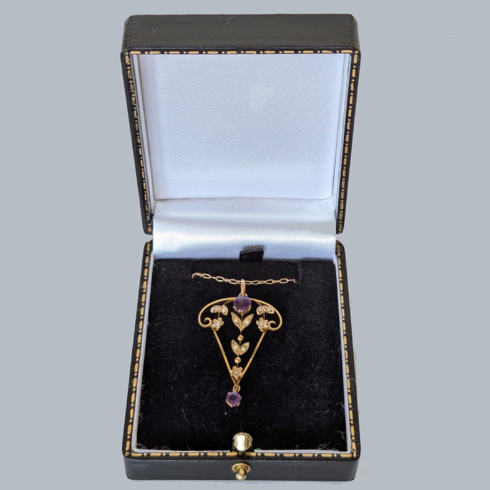An Edwardian 9ct gold openwork pendant featuring set seed pearls in a foliate motif with two round purple amethysts, suspended from a gold chain. View V