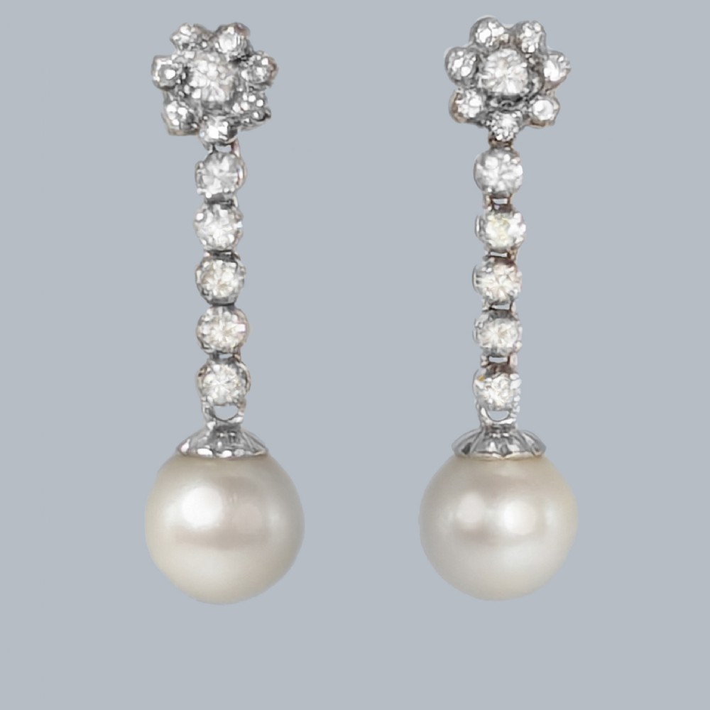 A pair of 1960s 18ct white gold drop earrings featuring floral diamond cluster tops above linear diamond links and round white pearls.