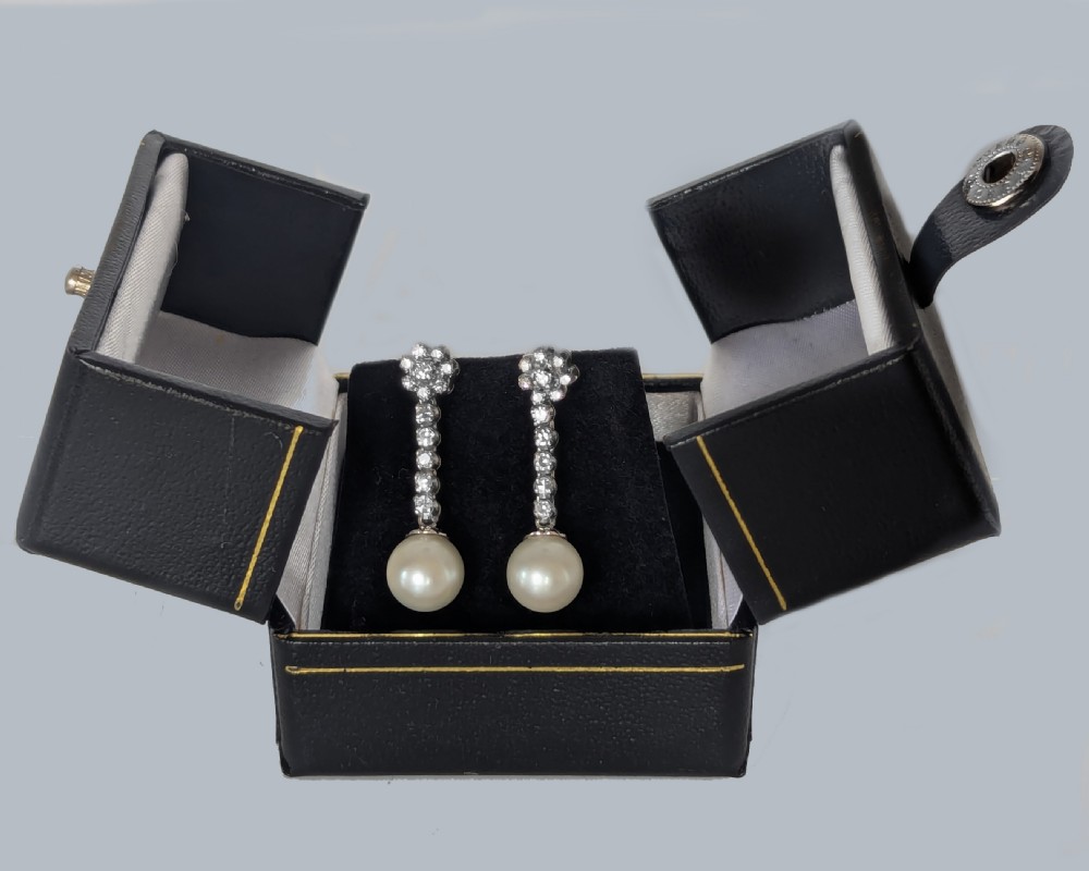 A pair of 1960s 18ct white gold drop earrings featuring floral diamond cluster tops above linear diamond links and round white pearls. View V