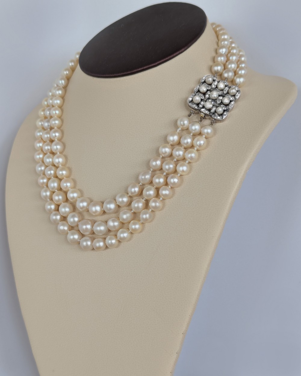 An Art Deco triple-strand cream pearl necklace featuring an ornate square clasp set with rose-cut diamonds and central pearl accents. View IV