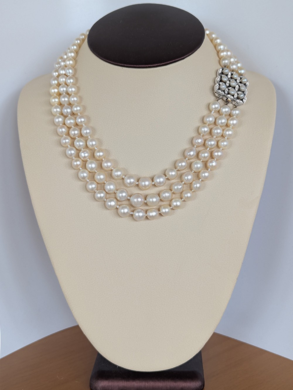 An Art Deco triple-strand cream pearl necklace featuring an ornate square clasp set with rose-cut diamonds and central pearl accents. View V