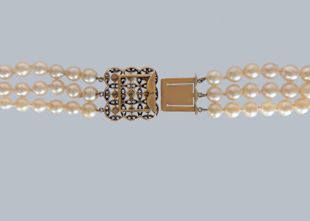 An Art Deco triple-strand cream pearl necklace featuring an ornate square clasp set with rose-cut diamonds and central pearl accents. View X