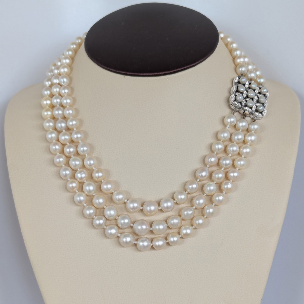 An Art Deco triple-strand cream pearl necklace featuring an ornate square clasp set with rose-cut diamonds and central pearl accents. View XV