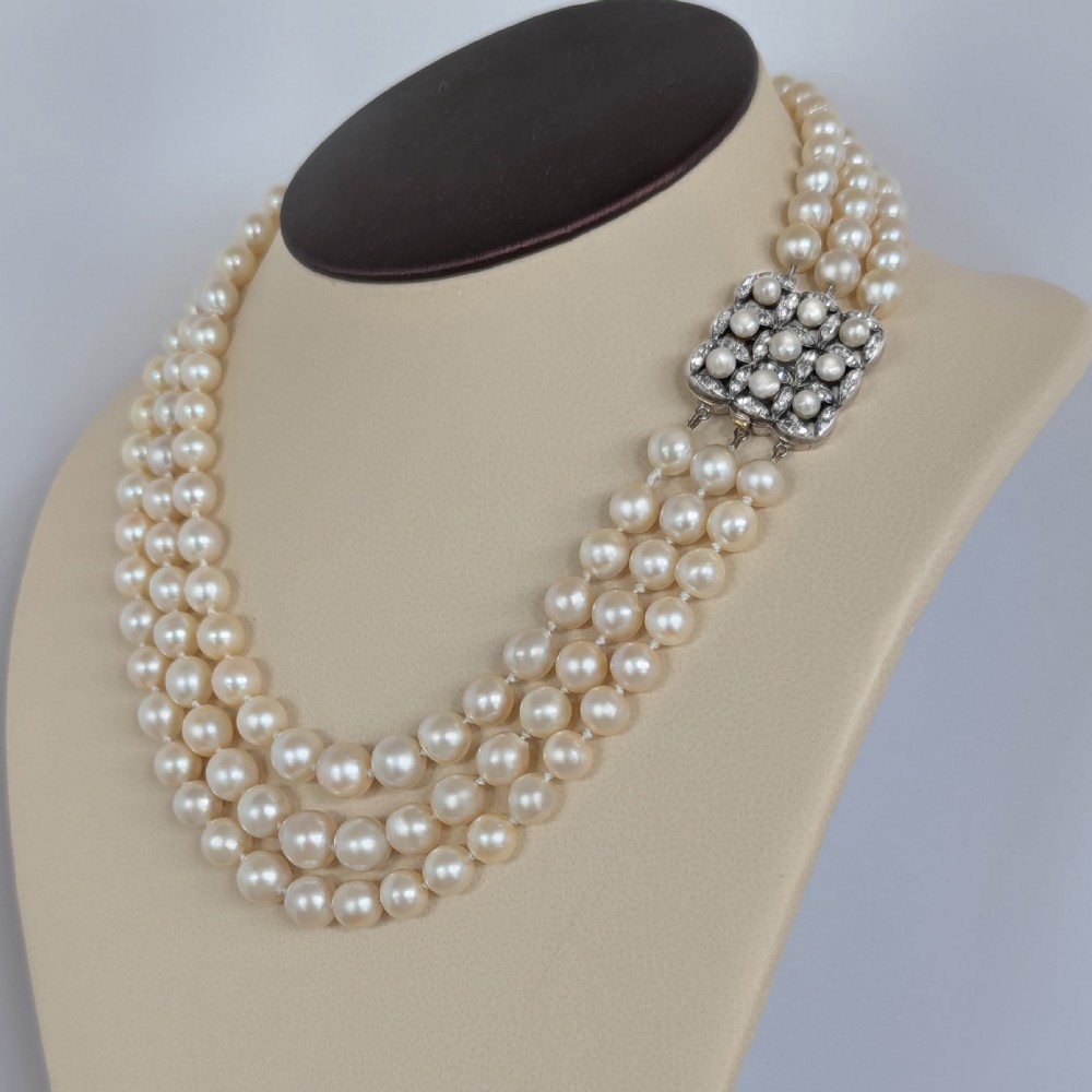 An Art Deco triple-strand cream pearl necklace featuring an ornate square clasp set with rose-cut diamonds and central pearl accents. View XVI