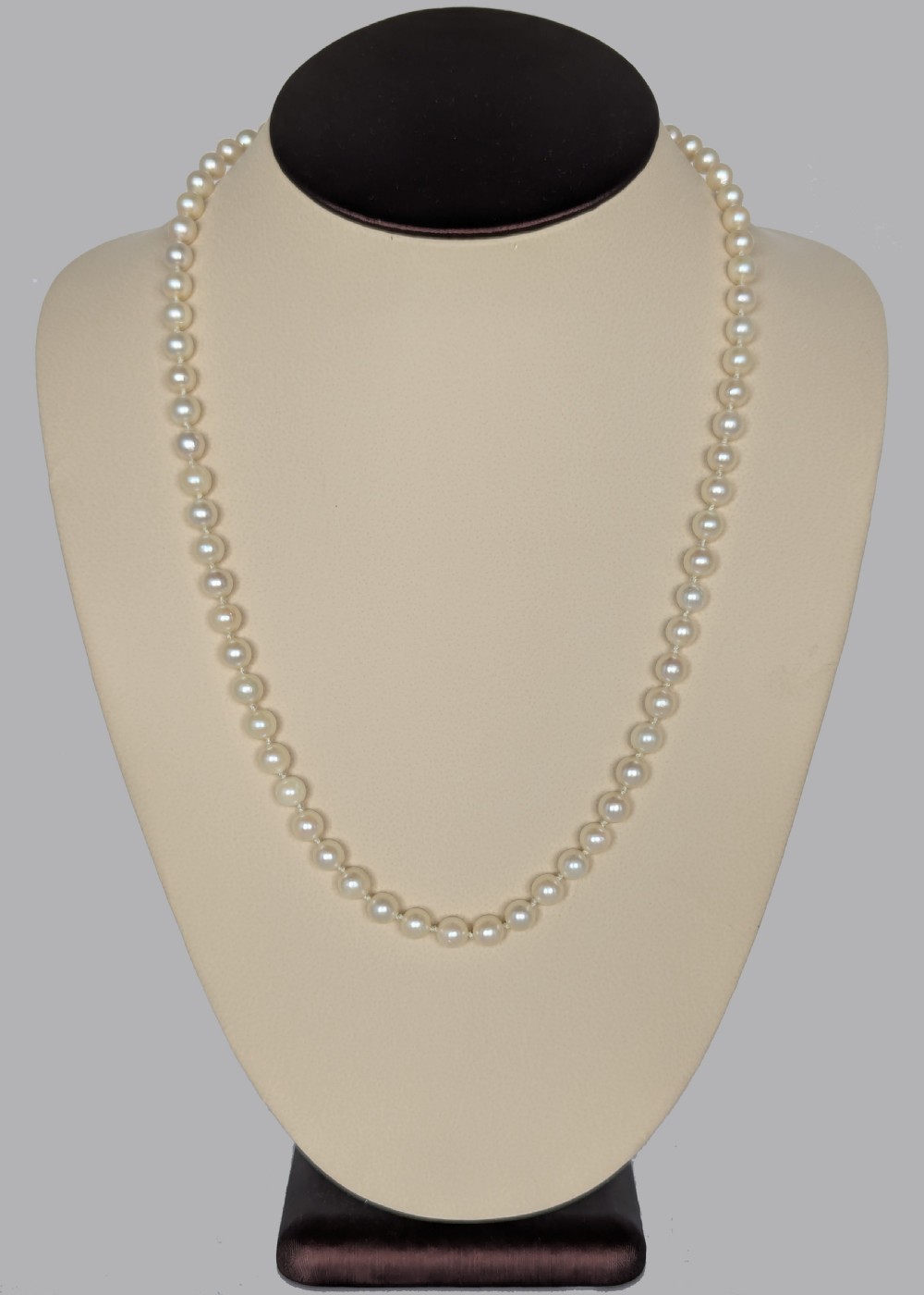 A single strand of uniform cream pearls featuring a central oval cabochon amethyst clasp set in gold, displayed against a black backdrop. View II