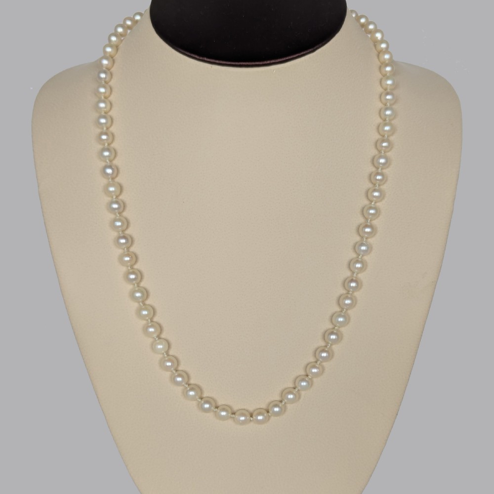 A single strand of uniform cream pearls featuring a central oval cabochon amethyst clasp set in gold, displayed against a black backdrop. View VI