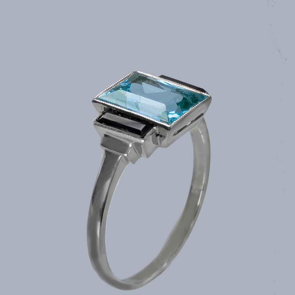 An 18ct white gold Art Deco ring featuring a central rectangular light blue spinel stone flanked by two vertical black onyx baguettes with millegrain borders. View VI