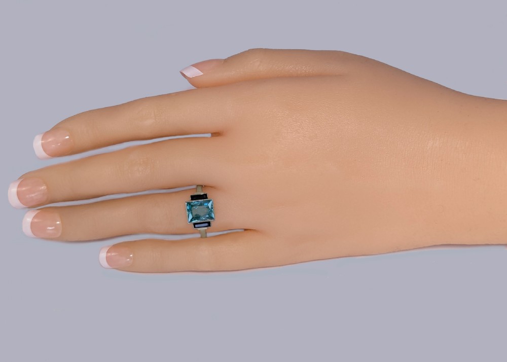 An 18ct white gold Art Deco ring featuring a central rectangular light blue spinel stone flanked by two vertical black onyx baguettes with millegrain borders. View XI