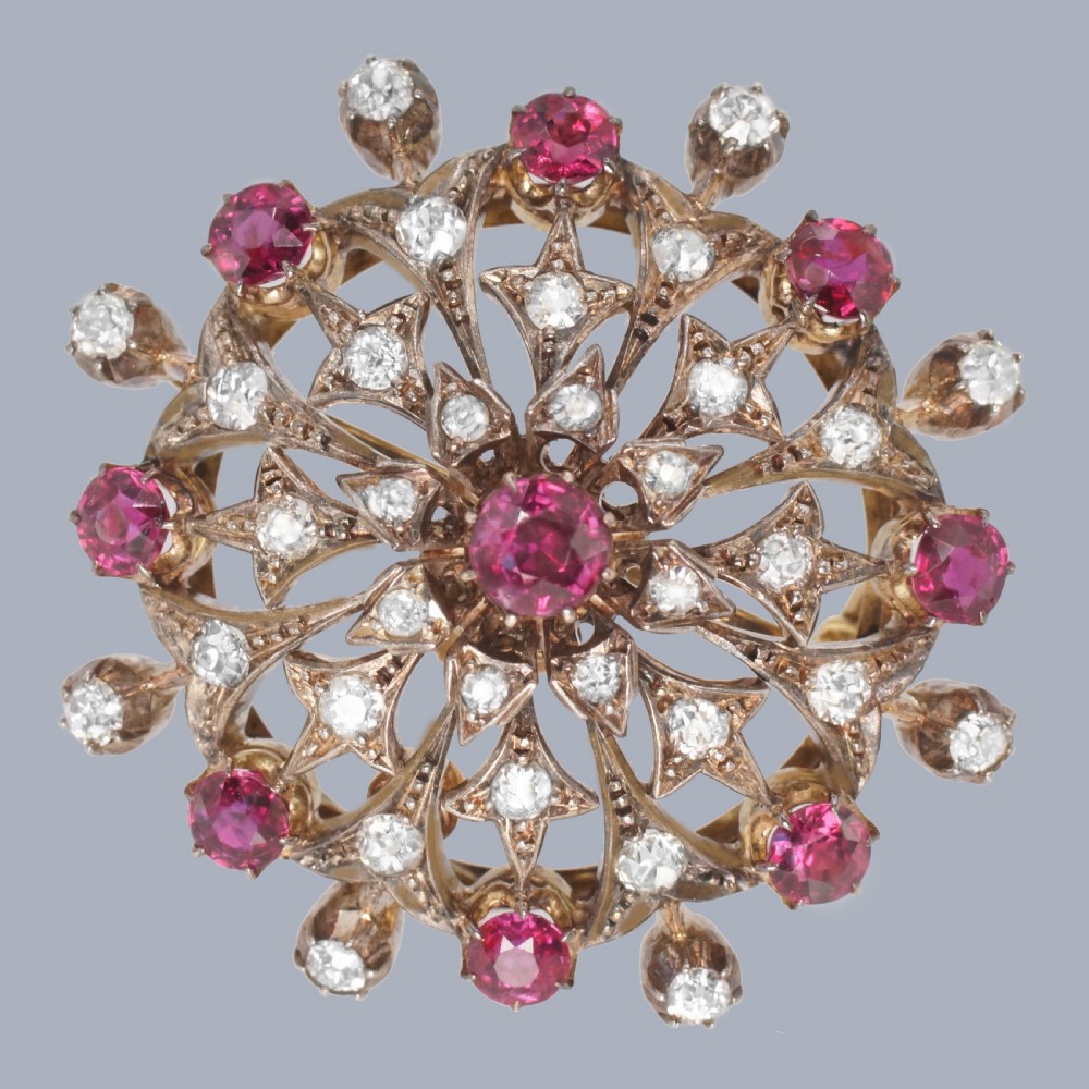 A circular Victorian starburst brooch featuring central and outer natural rubies surrounded by openwork diamond-set filigree.