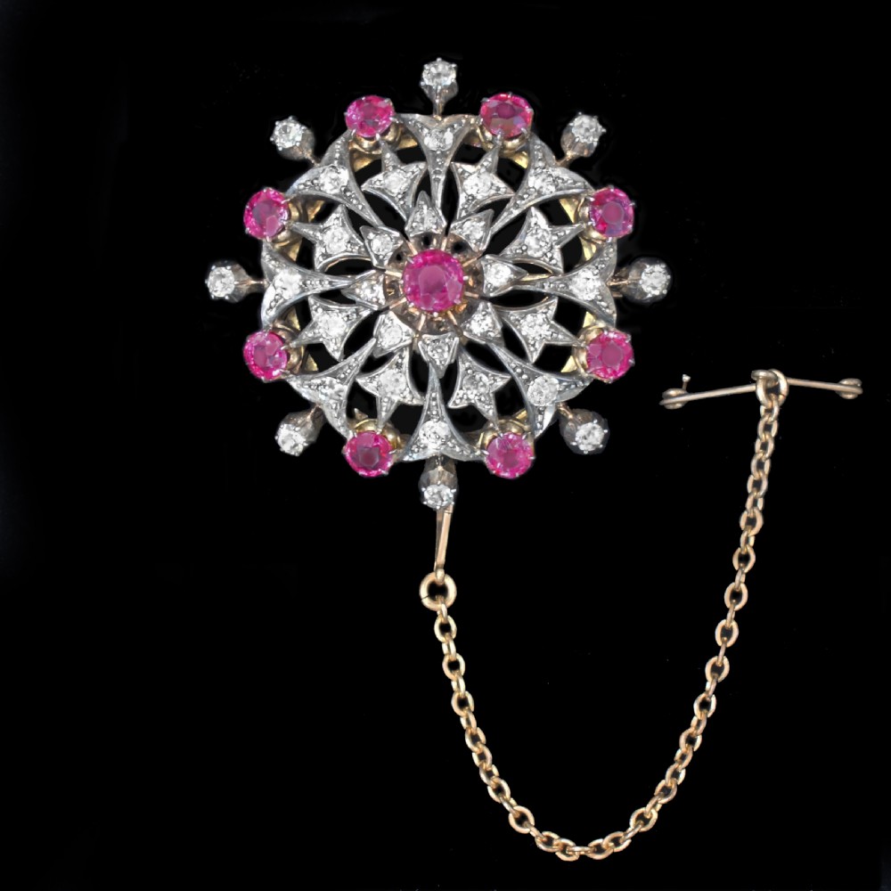 A circular Victorian starburst brooch featuring central and outer natural rubies surrounded by openwork diamond-set filigree. View II