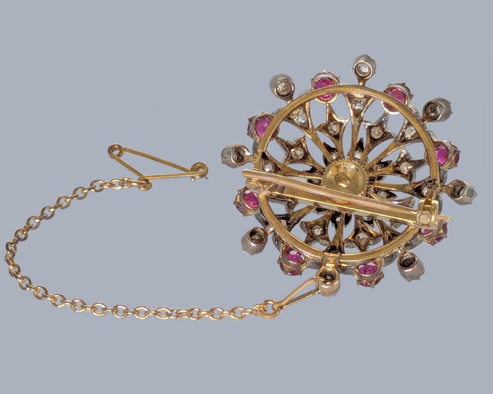 A circular Victorian starburst brooch featuring central and outer natural rubies surrounded by openwork diamond-set filigree. View V