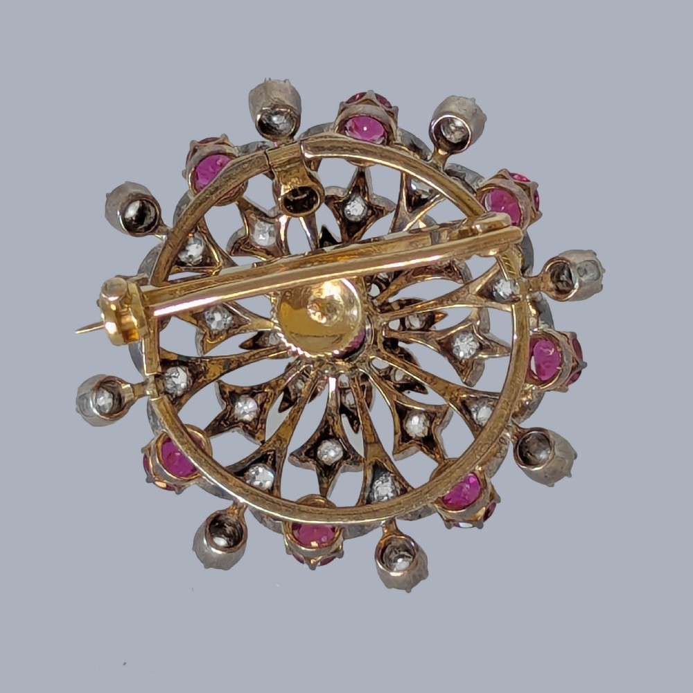 A circular Victorian starburst brooch featuring central and outer natural rubies surrounded by openwork diamond-set filigree. View VII