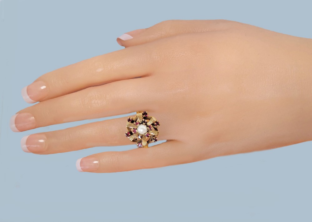 A 9ct yellow gold cluster ring featuring a central white pearl surrounded by textured gold ribbon loops set with round red rubies. View III