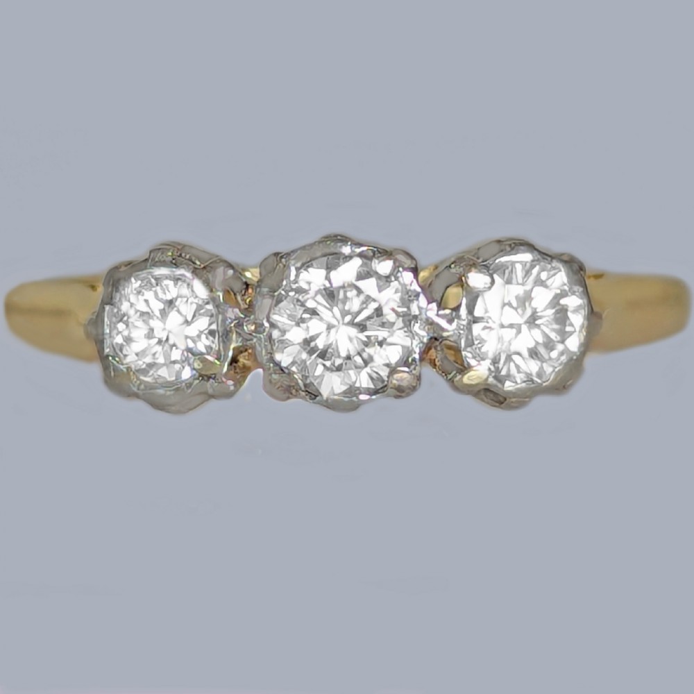 A three-stone round diamond trilogy ring set in white metal claw mounts on an 18ct yellow gold band.