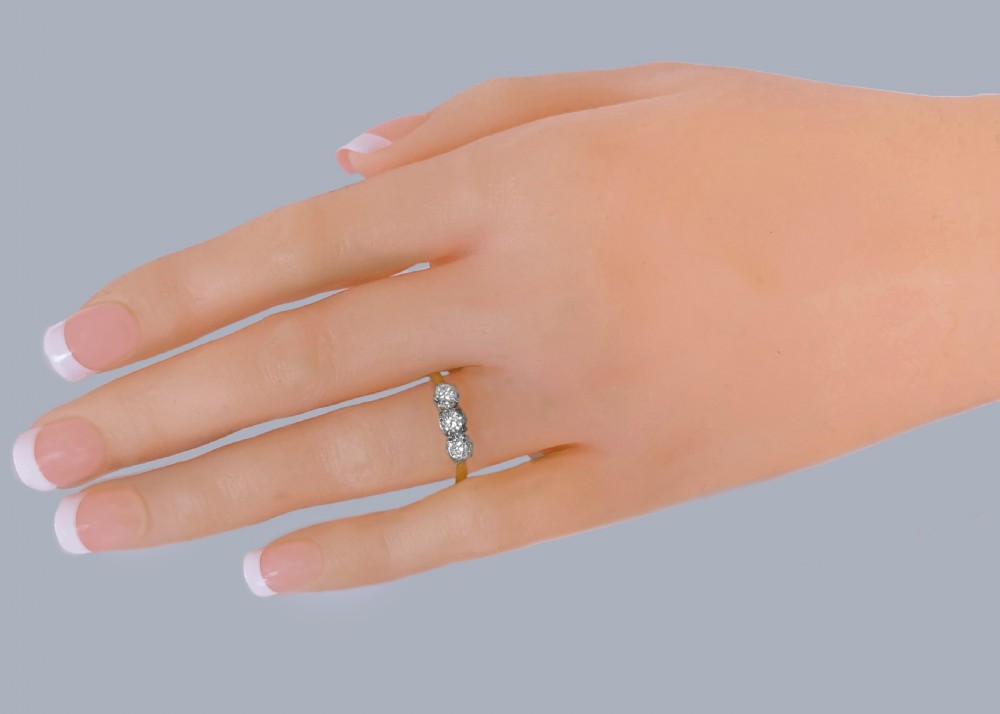 A three-stone round diamond trilogy ring set in white metal claw mounts on an 18ct yellow gold band. View II