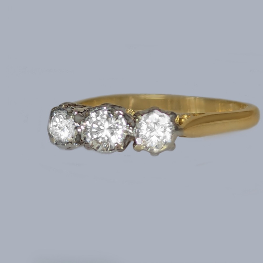 A three-stone round diamond trilogy ring set in white metal claw mounts on an 18ct yellow gold band. View IV