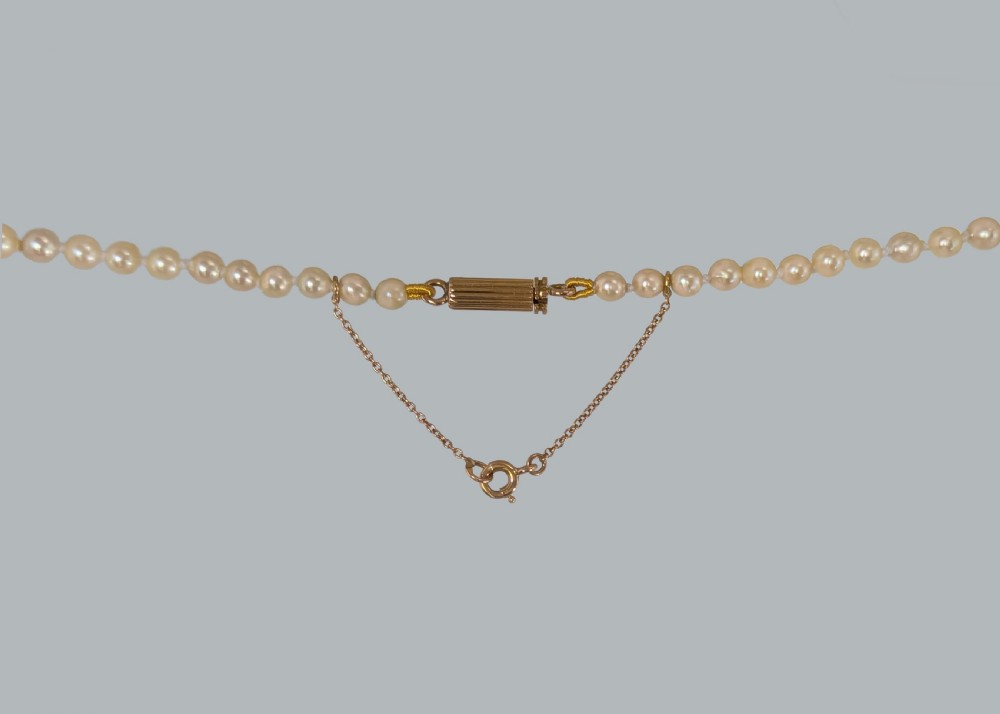 A single strand of graduated cream pearls featuring a fluted 18ct gold clasp and safety chain against a grey background. View III