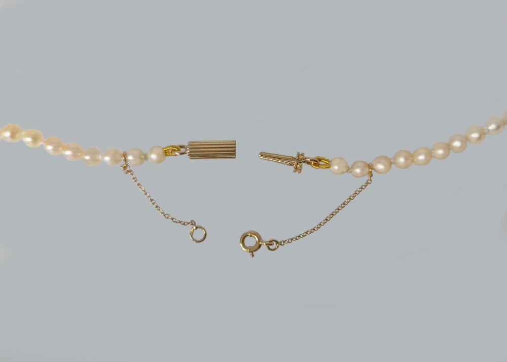 A single strand of graduated cream pearls featuring a fluted 18ct gold clasp and safety chain against a grey background. View IV