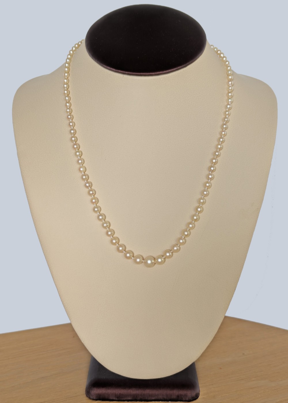 A single strand of graduated cream pearls featuring a fluted 18ct gold clasp and safety chain against a grey background. View V