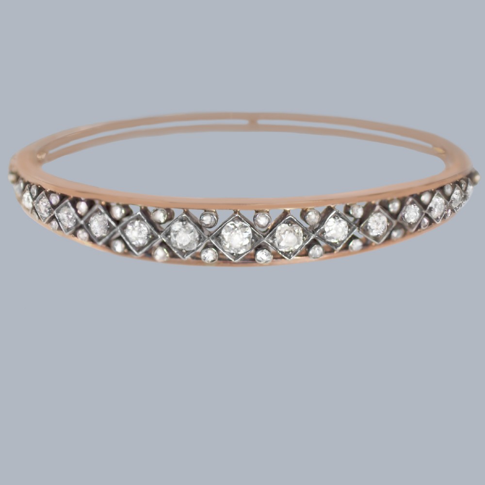 A Victorian 15ct gold and silver-topped hinged bangle set with a row of old mine cut diamonds in diamond-shaped mounts.