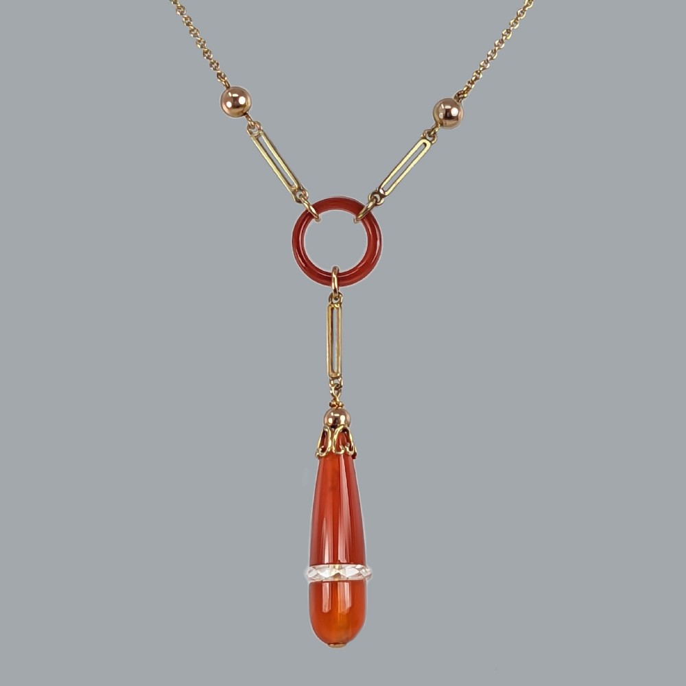 An Art Deco 9ct gold necklace featuring a central carnelian ring and an elongated carnelian drop pendant accented with a band of faceted rock crystal.