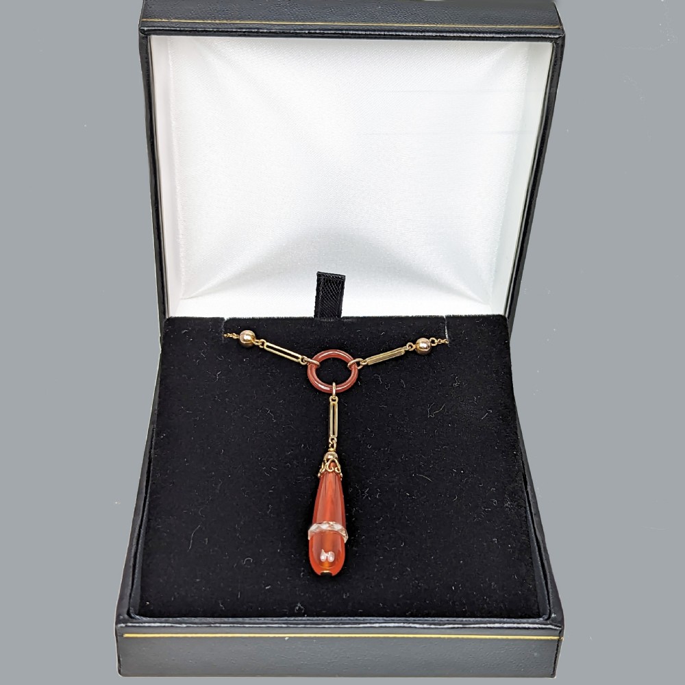 An Art Deco 9ct gold necklace featuring a central carnelian ring and an elongated carnelian drop pendant accented with a band of faceted rock crystal. View IV