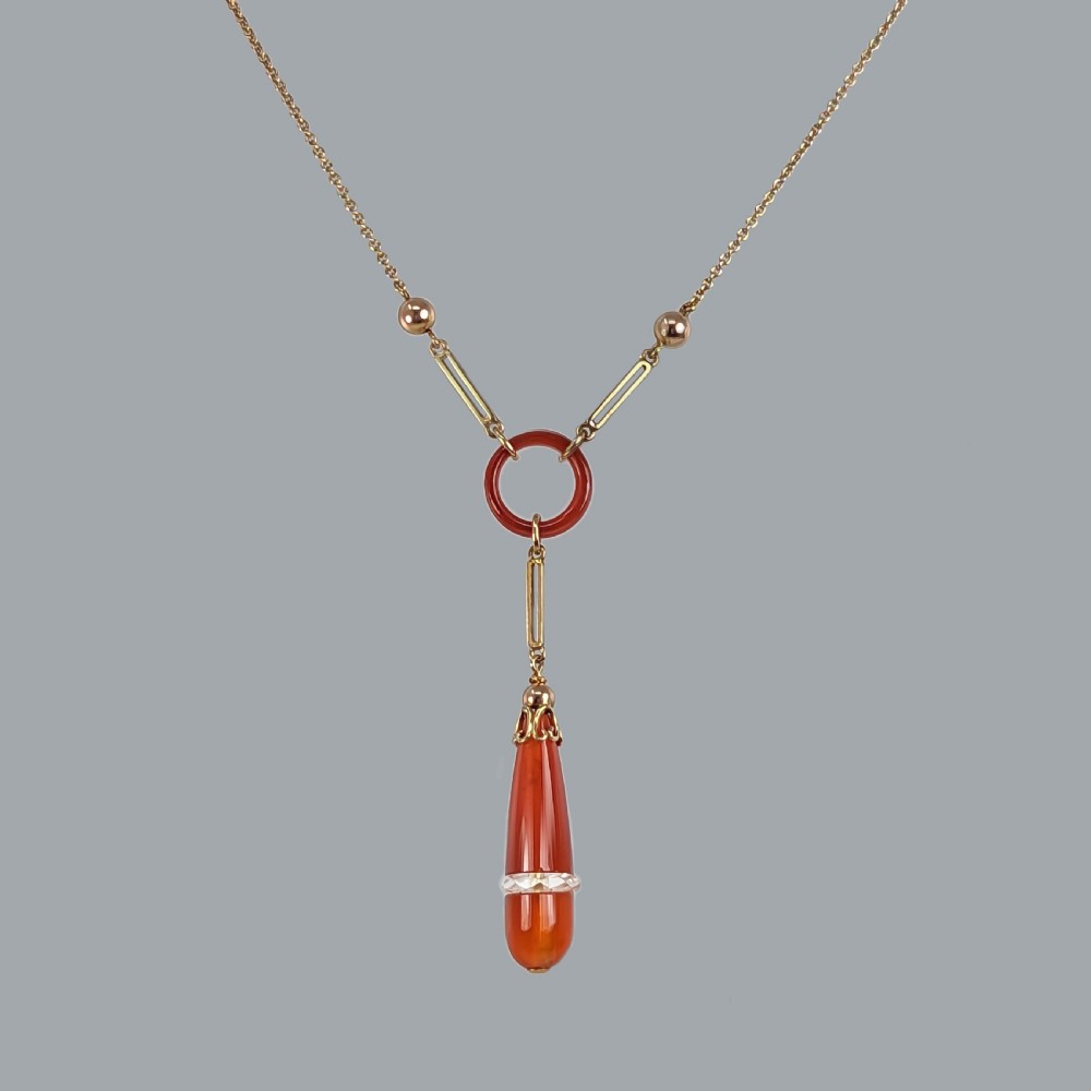 An Art Deco 9ct gold necklace featuring a central carnelian ring and an elongated carnelian drop pendant accented with a band of faceted rock crystal. View V