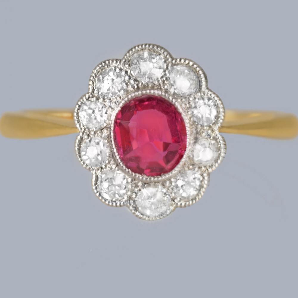 A vintage cluster ring featuring a central oval red ruby surrounded by ten round diamonds set in platinum with an 18ct yellow gold band.