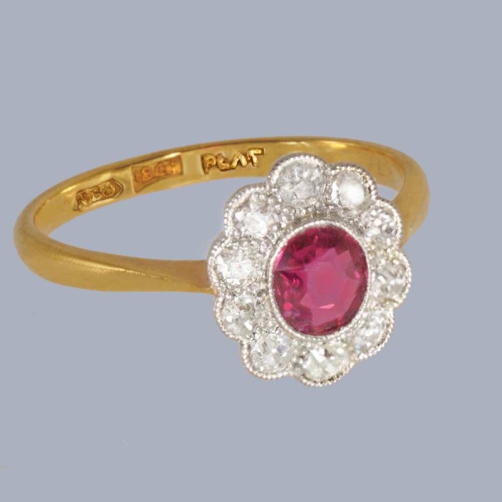 A vintage cluster ring featuring a central oval red ruby surrounded by ten round diamonds set in platinum with an 18ct yellow gold band. View IV