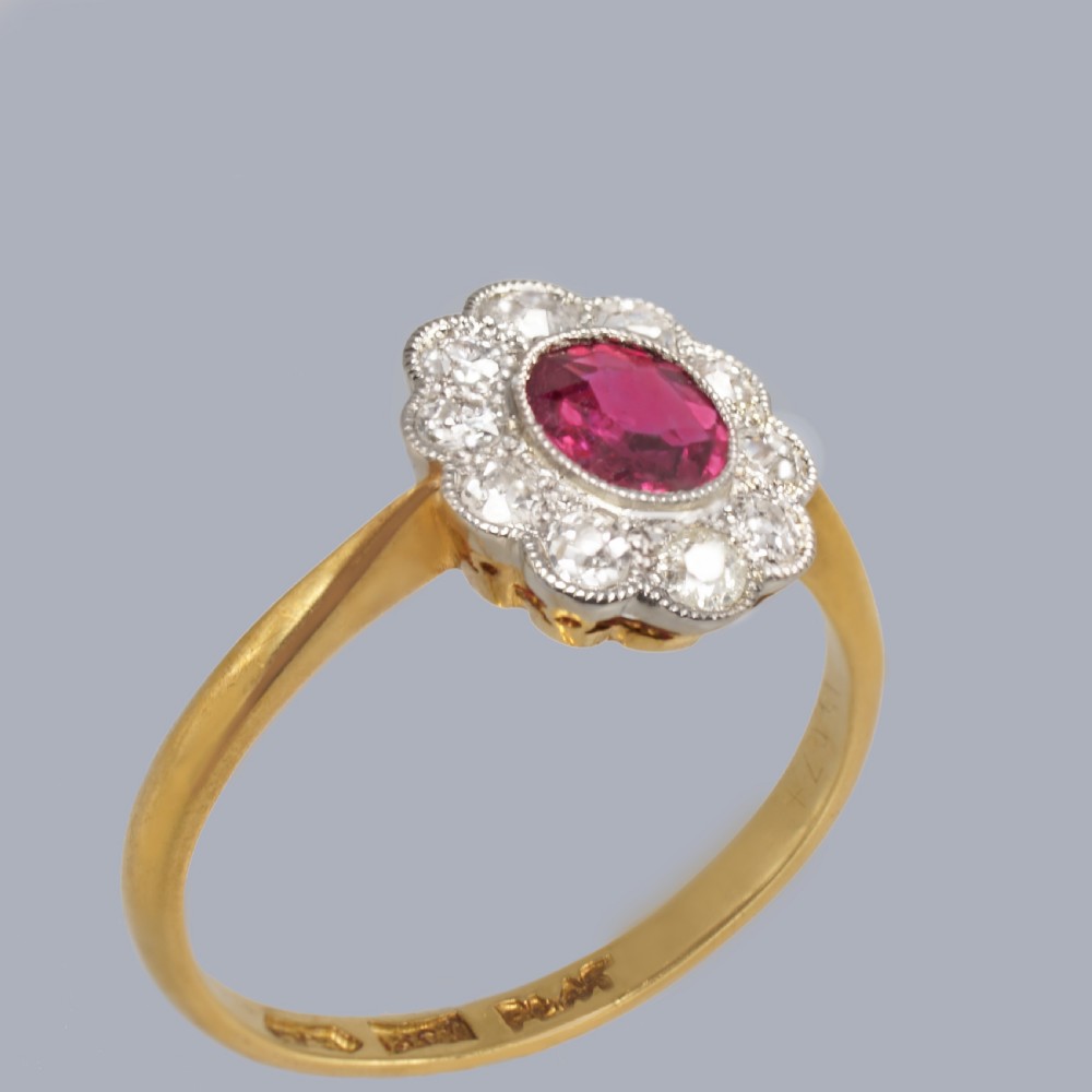 A vintage cluster ring featuring a central oval red ruby surrounded by ten round diamonds set in platinum with an 18ct yellow gold band. View V