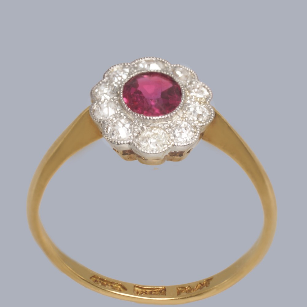 A vintage cluster ring featuring a central oval red ruby surrounded by ten round diamonds set in platinum with an 18ct yellow gold band. View VI