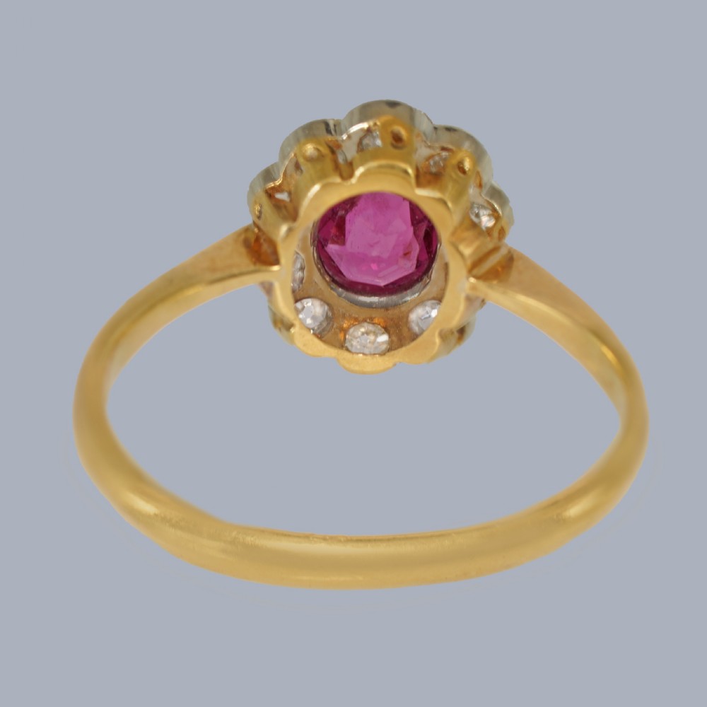 A vintage cluster ring featuring a central oval red ruby surrounded by ten round diamonds set in platinum with an 18ct yellow gold band. View X