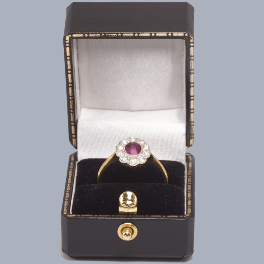 A vintage cluster ring featuring a central oval red ruby surrounded by ten round diamonds set in platinum with an 18ct yellow gold band. View XI