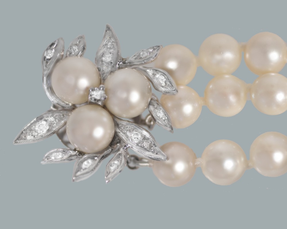 A vintage triple strand cultured pearl bracelet featuring a white gold floral clasp set with small diamonds and central pearls. View V