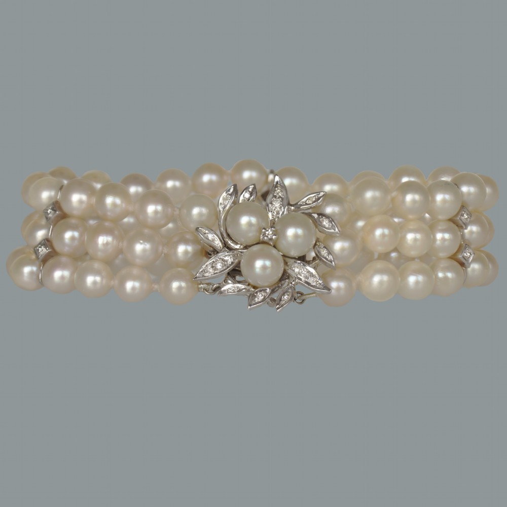 A vintage triple strand cultured pearl bracelet featuring a white gold floral clasp set with small diamonds and central pearls.