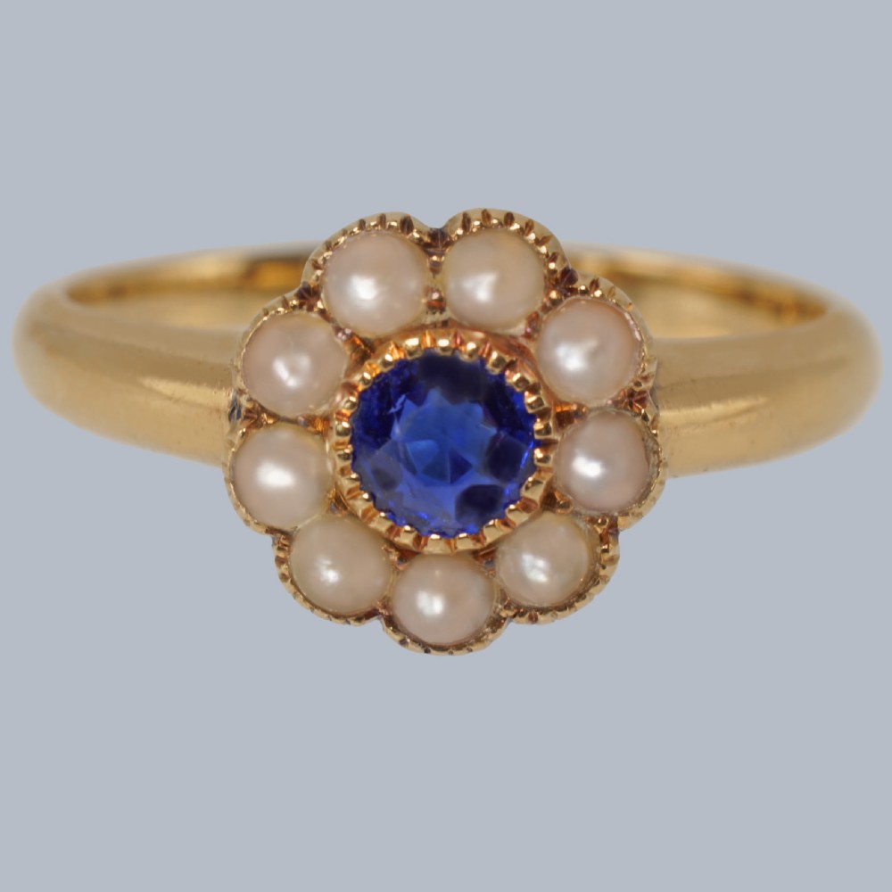 An 18ct yellow gold Victorian cluster ring featuring a central round blue sapphire encircled by eight split pearls.