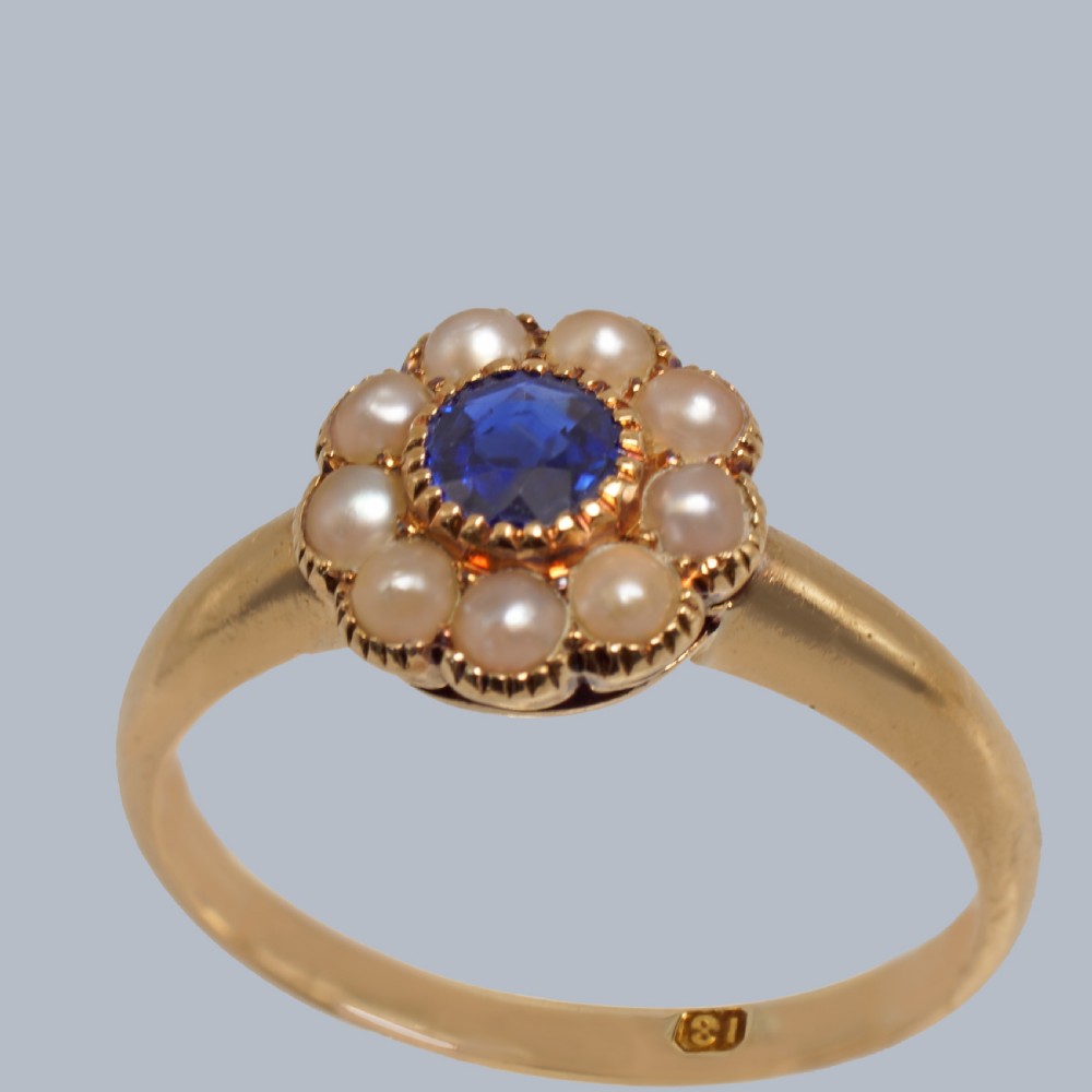 An 18ct yellow gold Victorian cluster ring featuring a central round blue sapphire encircled by eight split pearls. View IV