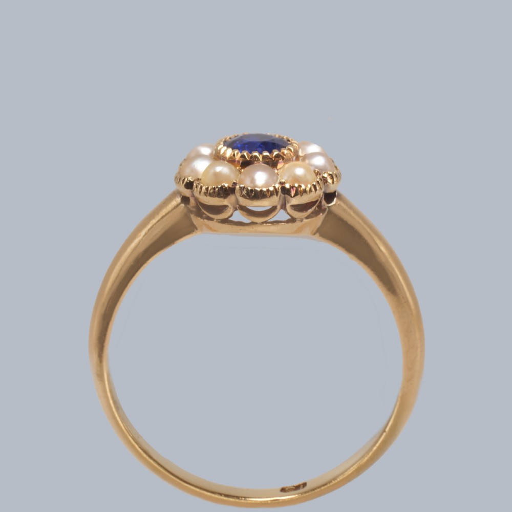 An 18ct yellow gold Victorian cluster ring featuring a central round blue sapphire encircled by eight split pearls. View V