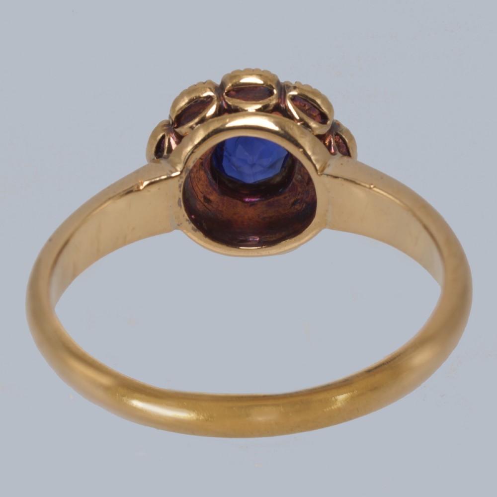 An 18ct yellow gold Victorian cluster ring featuring a central round blue sapphire encircled by eight split pearls. View VI