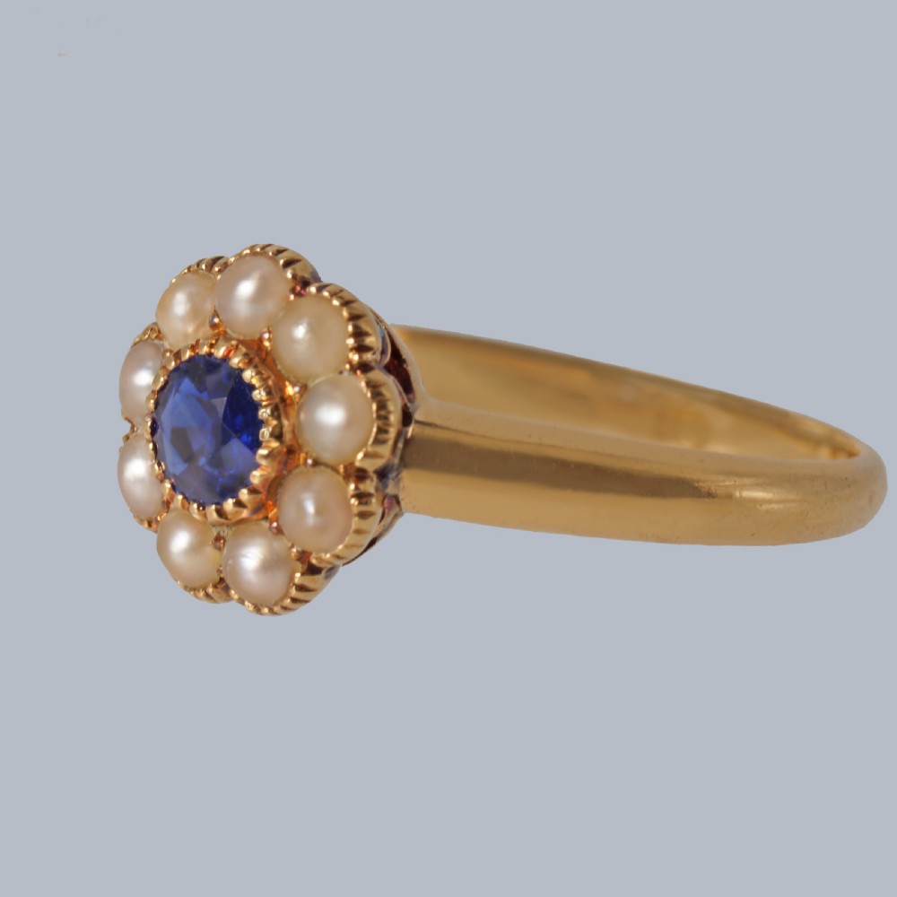 An 18ct yellow gold Victorian cluster ring featuring a central round blue sapphire encircled by eight split pearls. View VIII