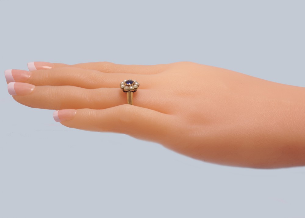 An 18ct yellow gold Victorian cluster ring featuring a central round blue sapphire encircled by eight split pearls. View X
