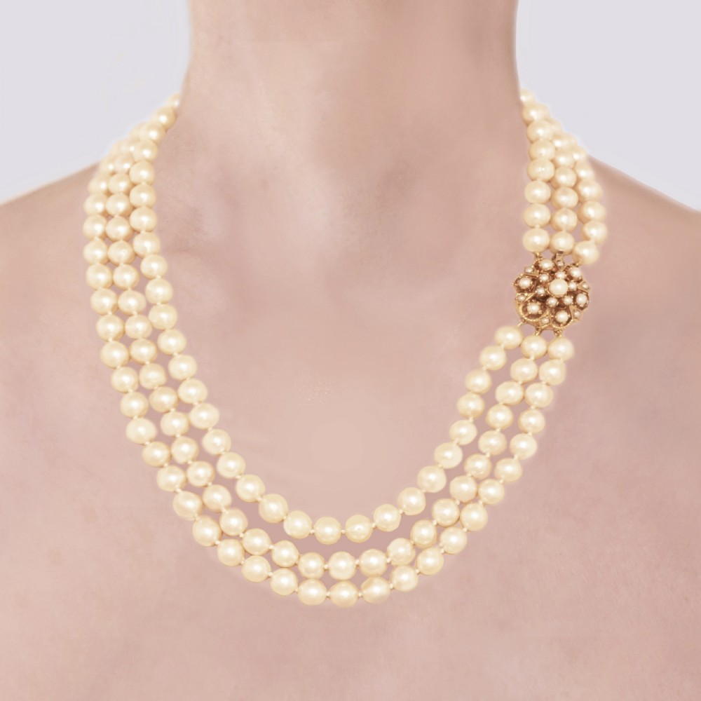 A 1960s triple strand cultured pearl necklace featuring cream-coloured pearls and a 9ct gold floral cluster clasp.