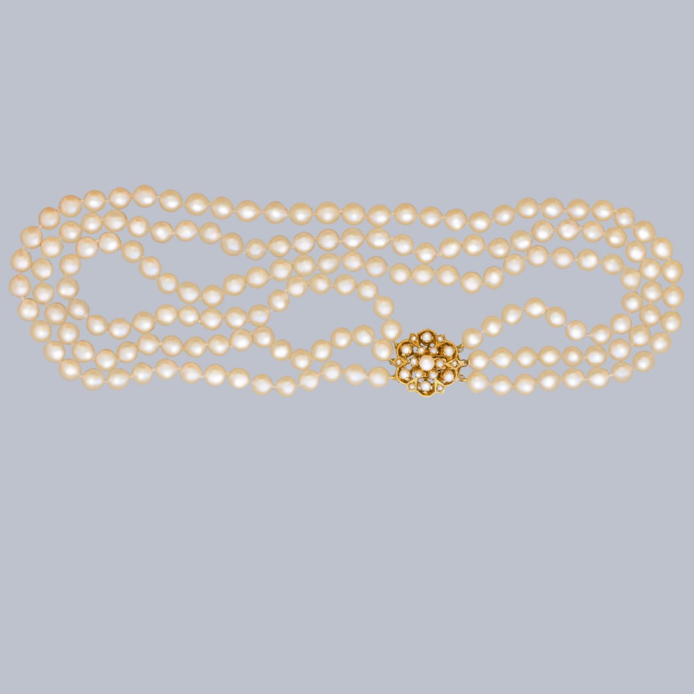 A 1960s triple strand cultured pearl necklace featuring cream-coloured pearls and a 9ct gold floral cluster clasp. View II