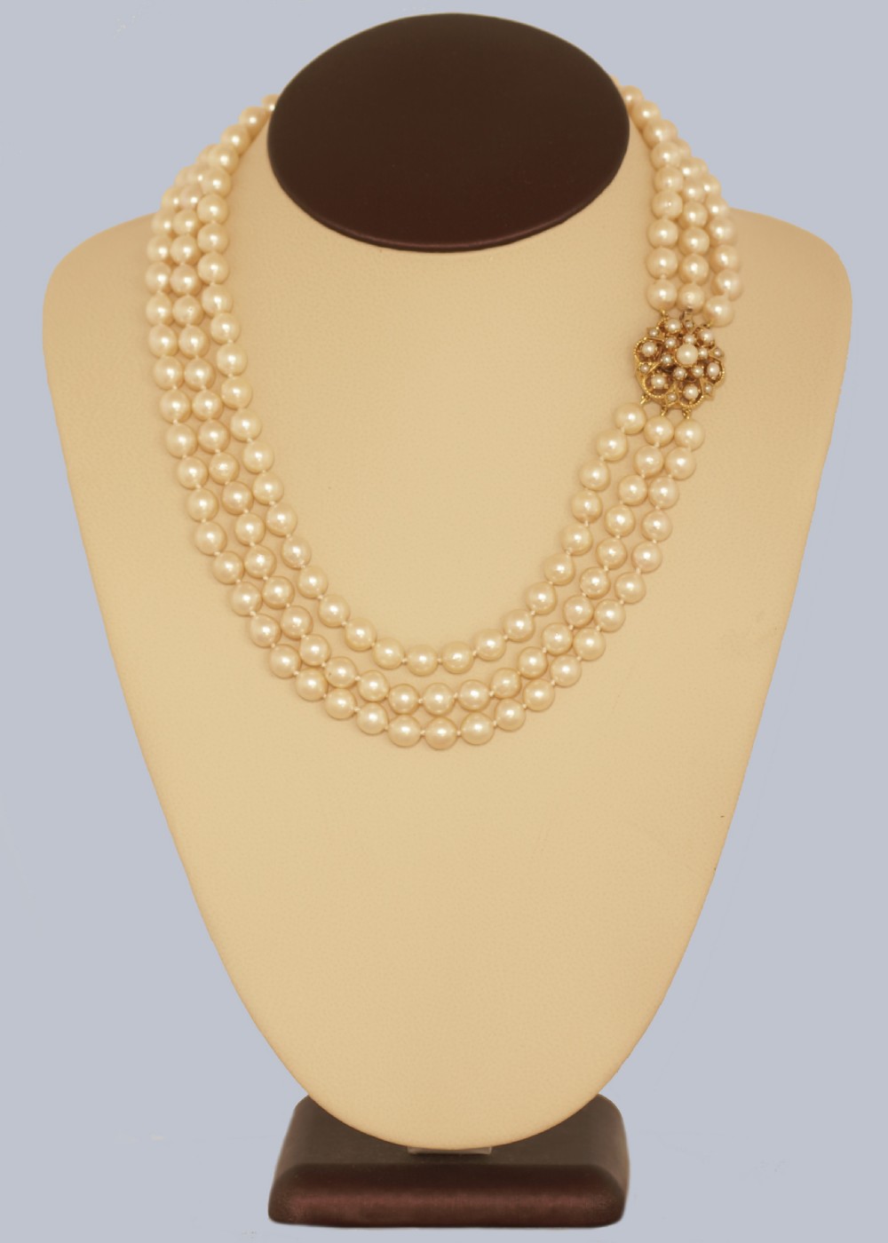 A 1960s triple strand cultured pearl necklace featuring cream-coloured pearls and a 9ct gold floral cluster clasp. View IV