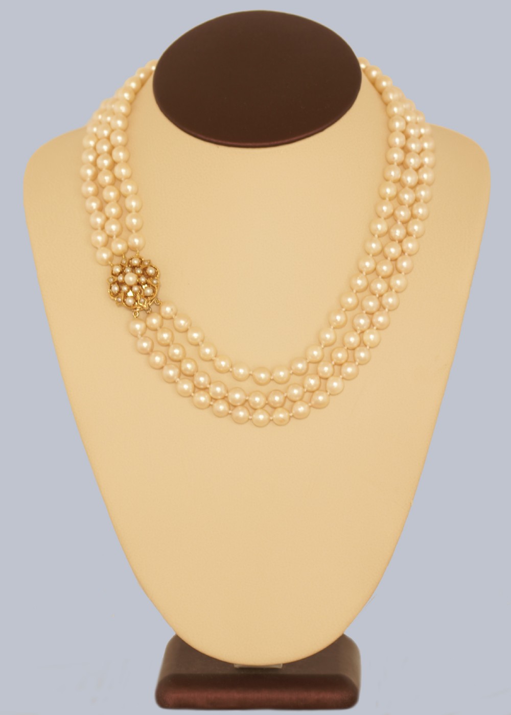 A 1960s triple strand cultured pearl necklace featuring cream-coloured pearls and a 9ct gold floral cluster clasp. View V