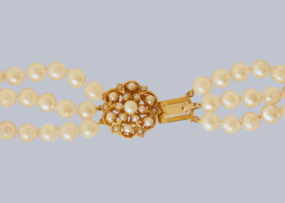 A 1960s triple strand cultured pearl necklace featuring cream-coloured pearls and a 9ct gold floral cluster clasp. View VI