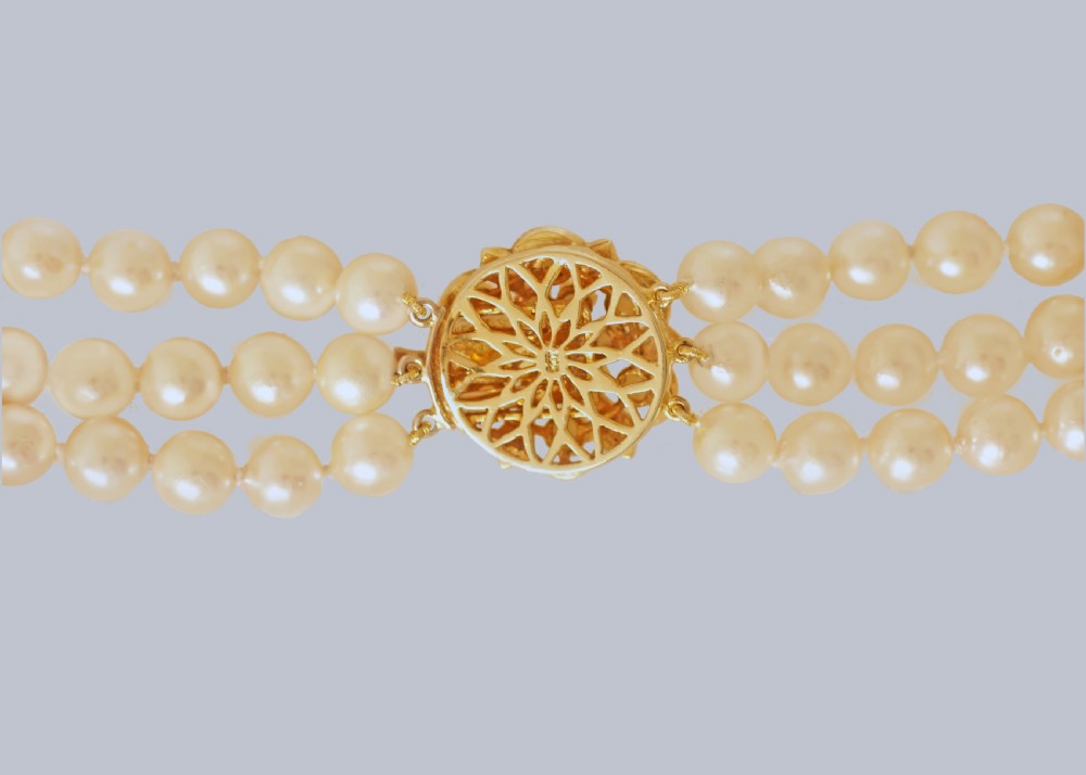 A 1960s triple strand cultured pearl necklace featuring cream-coloured pearls and a 9ct gold floral cluster clasp. View VII