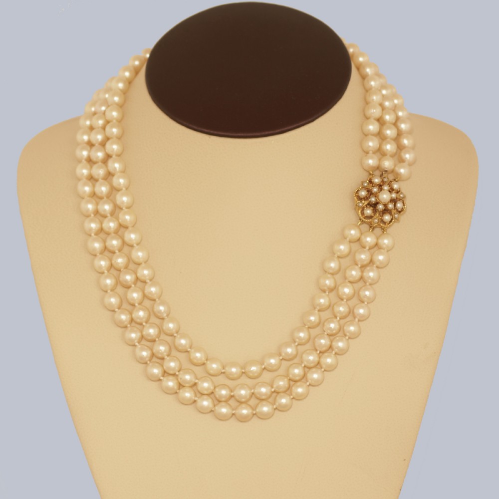 A 1960s triple strand cultured pearl necklace featuring cream-coloured pearls and a 9ct gold floral cluster clasp. View XI